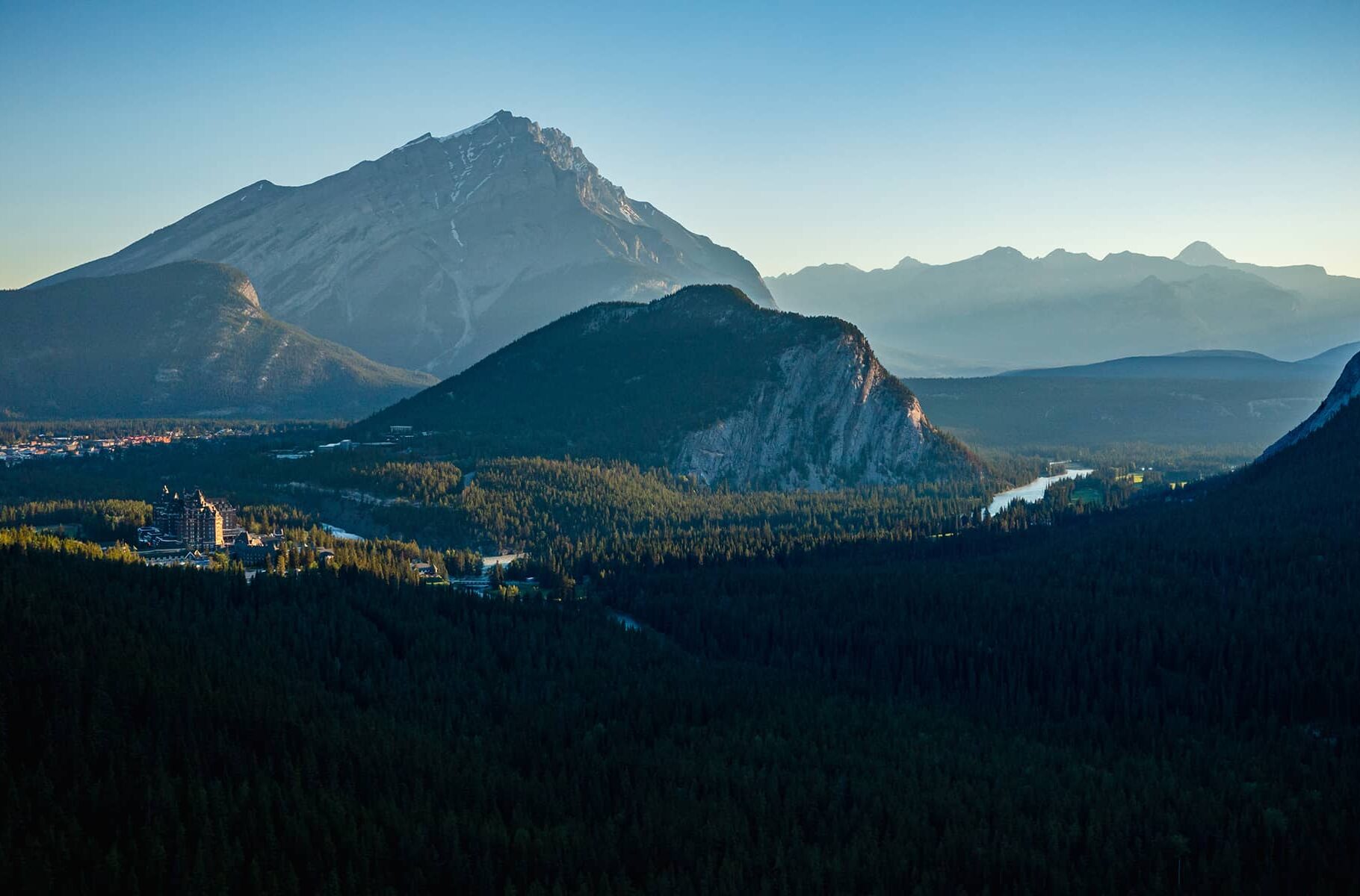 A sweeping view of Banff at sunrise, featuring Cascade Mountain towering behind Tunnel Mountain, with the Bow River valley illuminated by soft morning light.