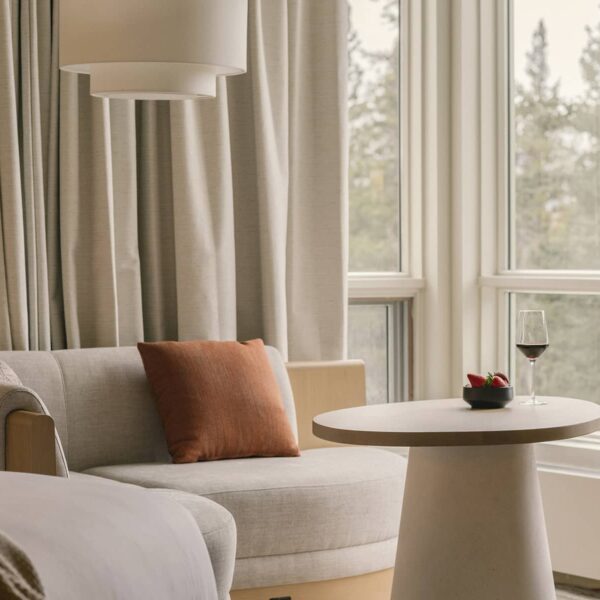 en::A cozy window nook overlooking a serene forest, perfect for relaxing with a glass of wine| fr::Une alcôve confortable avec vue sur la forêt sereine, parfaite pour se détendre avec un verre de vin| es::Un acogedor rincón junto a la ventana con vista a un sereno bosque, que crea un espacio perfecto para relajarse con una copa de vino