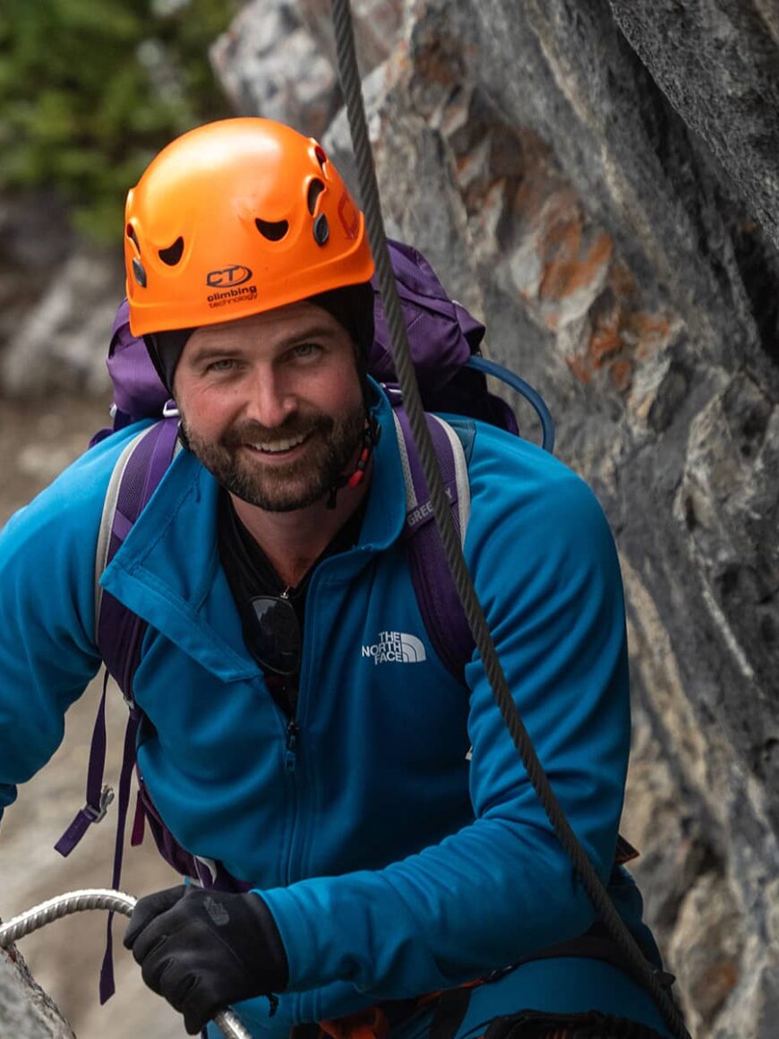 Harnessed climber pauses along Mount Norquay’s Via Ferrata, steady on iron rungs with rock walls rising around him.