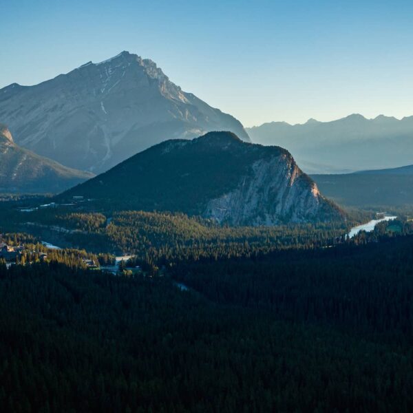 A sweeping view of Banff at sunrise, featuring Cascade Mountain towering behind Tunnel Mountain, with the Bow River valley illuminated by soft morning light.