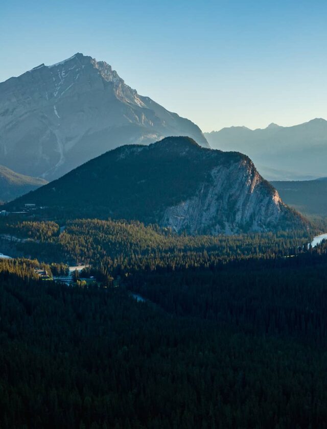 A sweeping view of Banff at sunrise, featuring Cascade Mountain towering behind Tunnel Mountain, with the Bow River valley illuminated by soft morning light.