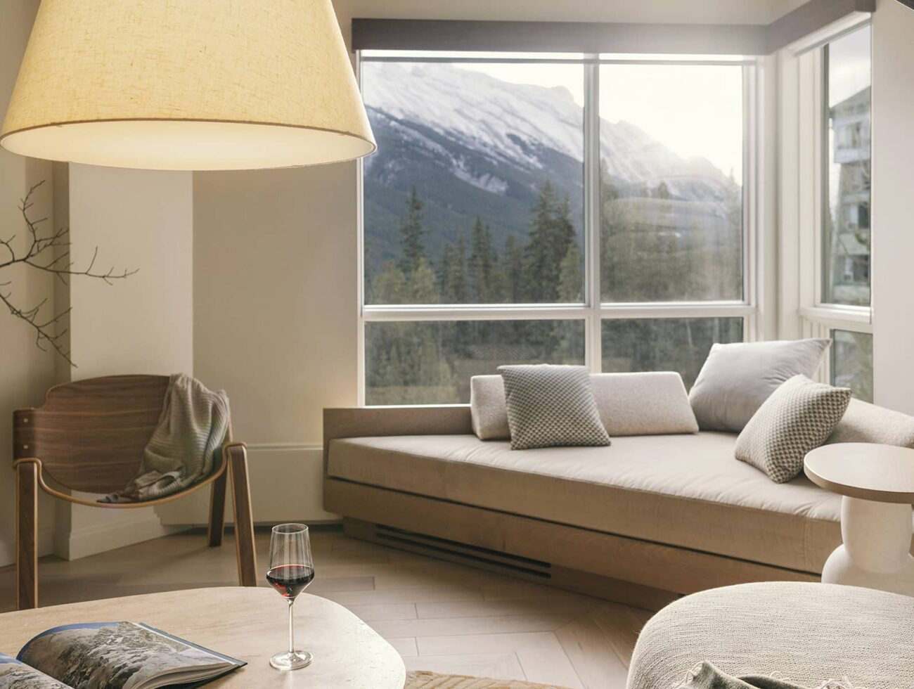 A bright living space in a Rimrock Banff one-bedroom suite featuring soft neutral furnishings, warm natural light, and mountain views framed by large windows.