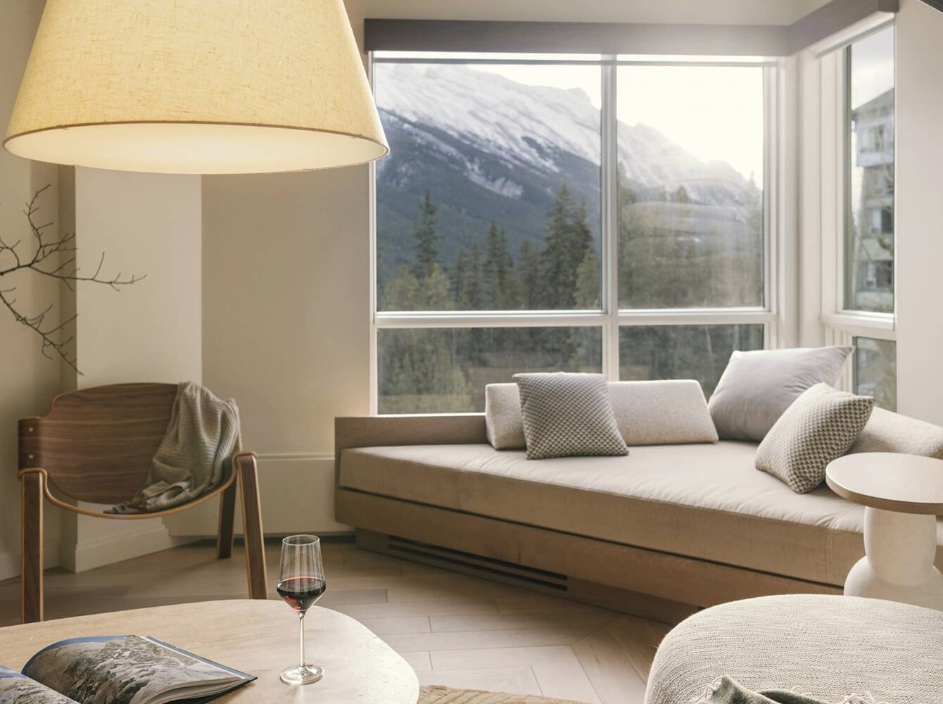 A bright living space in a Rimrock Banff one-bedroom suite featuring soft neutral furnishings, warm natural light, and mountain views framed by large windows.