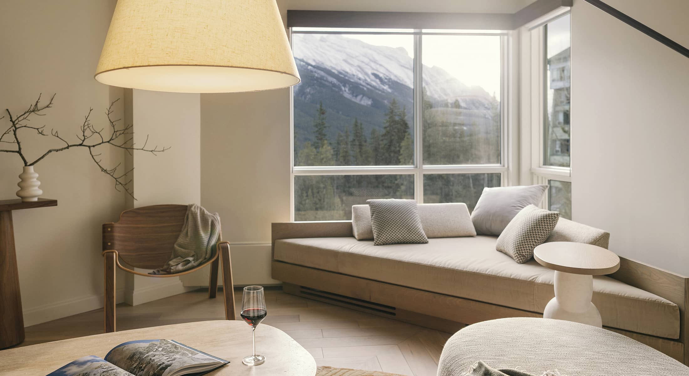 A bright living space in a Rimrock Banff one-bedroom suite featuring soft neutral furnishings, warm natural light, and mountain views framed by large windows.