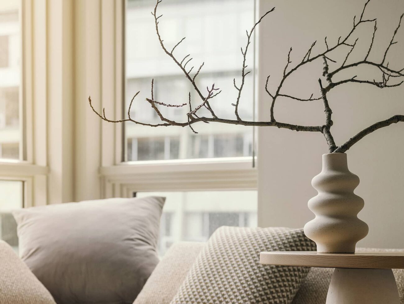 A bright seating nook in a Rimrock Banff one-bedroom suite featuring soft neutral pillows, natural light, and a sculptural vase with minimalist branches.
