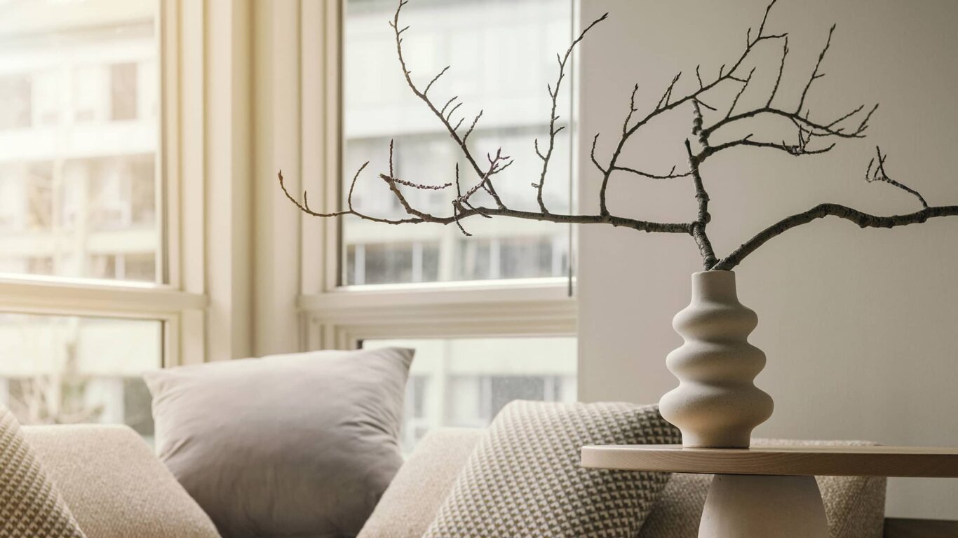 A bright seating nook in a Rimrock Banff one-bedroom suite featuring soft neutral pillows, natural light, and a sculptural vase with minimalist branches.