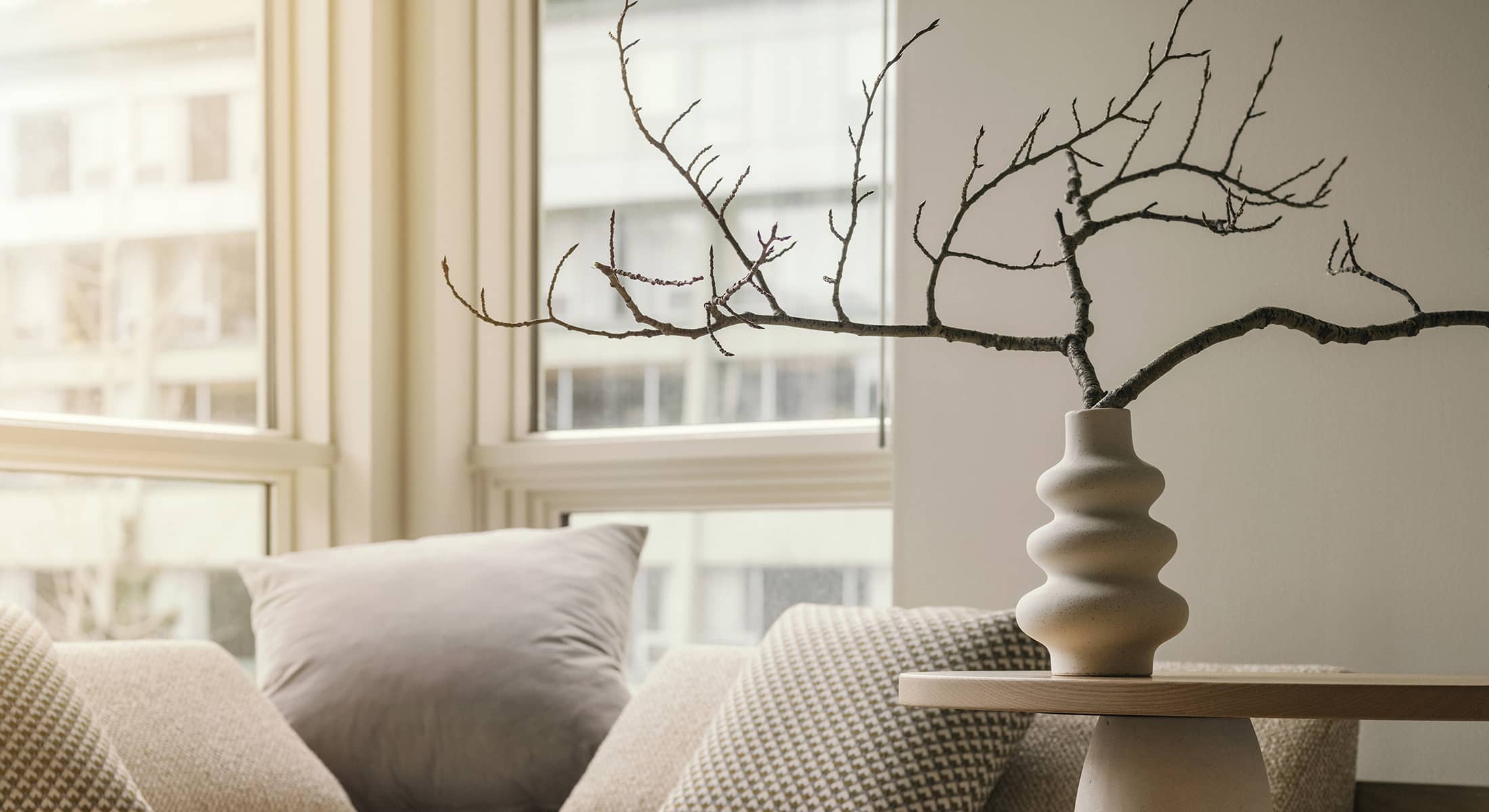 A bright seating nook in a Rimrock Banff one-bedroom suite featuring soft neutral pillows, natural light, and a sculptural vase with minimalist branches.
