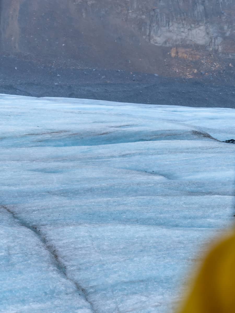 Close-up view of the Athabasca Glacier surface, showing layered blue ice and natural fractures formed by glacial movement.
