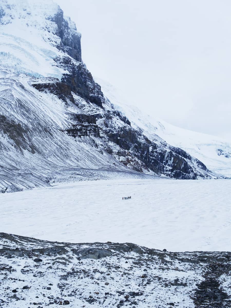 Small group walking across the Athabasca Glacier, surrounded by expansive ice and steep mountain walls.