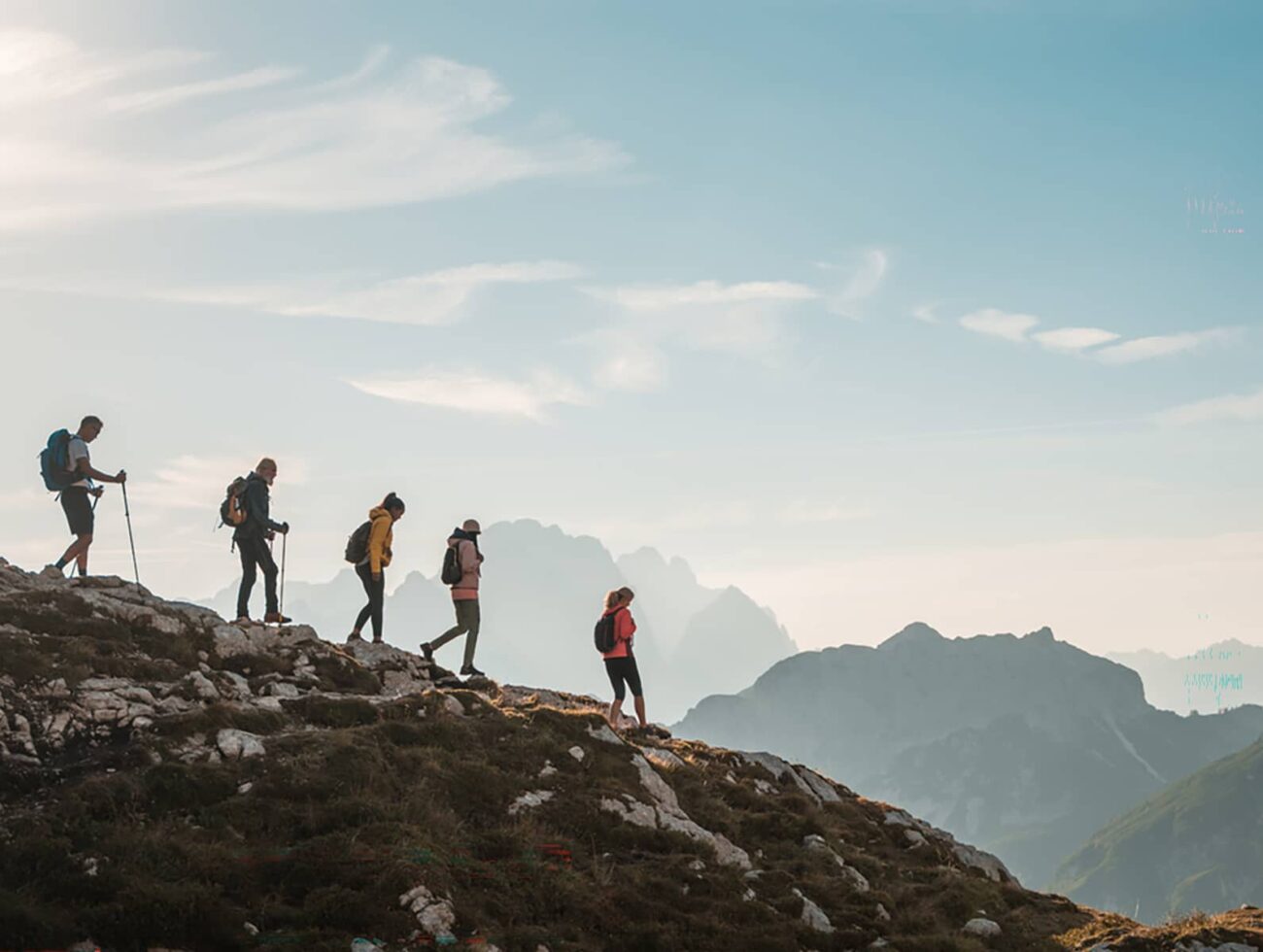 Small group hiking along a rocky alpine ridge in Banff National Park with layered mountain silhouettes in the distance.