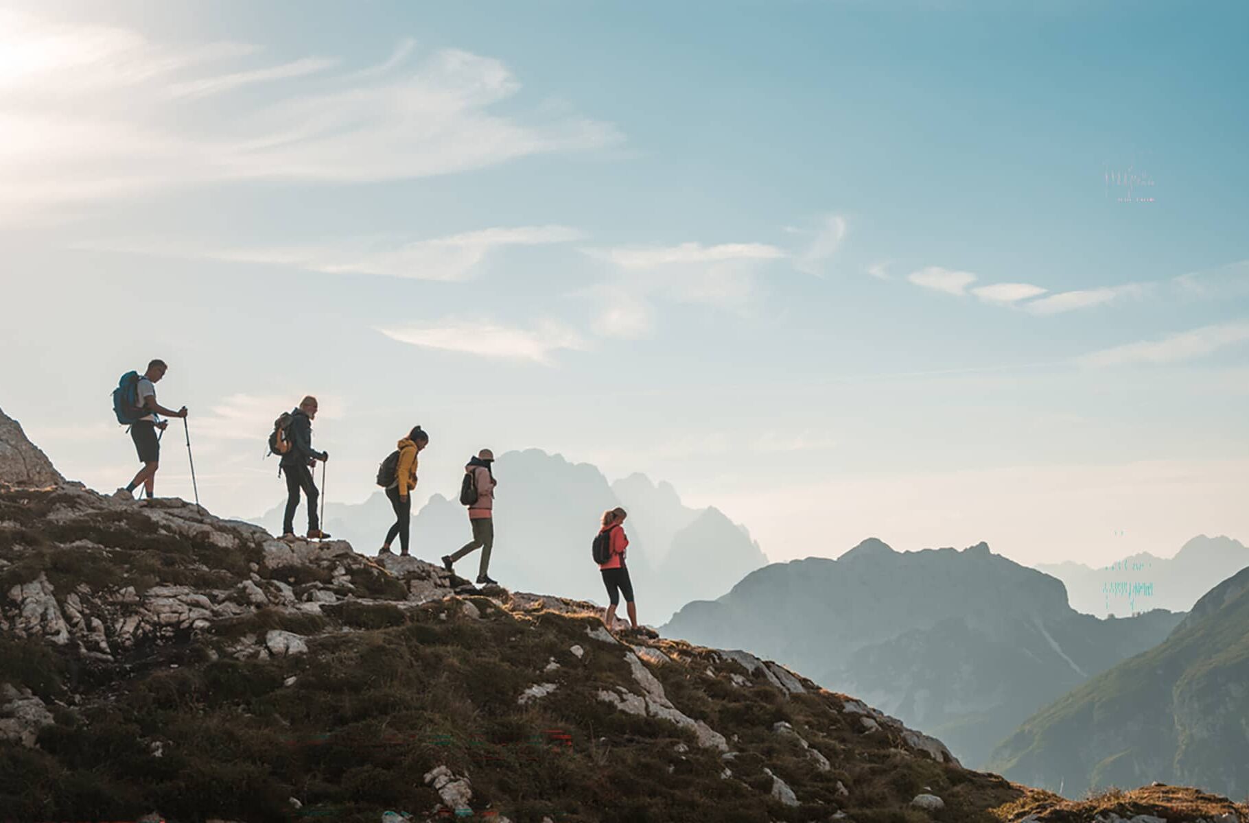 Small group hiking along a rocky alpine ridge in Banff National Park with layered mountain silhouettes in the distance.
