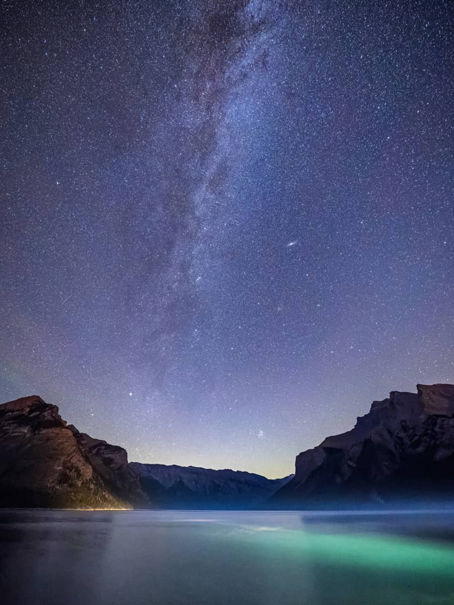 The Milky Way stretching across the night sky above Lake Minnewanka, framed by dark mountain silhouettes.