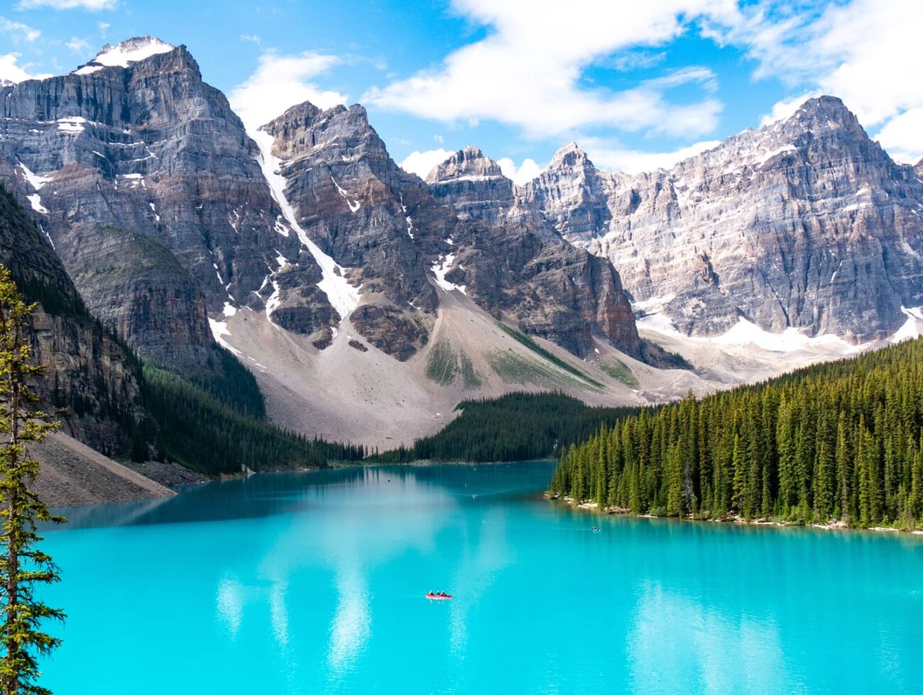 Turquoise waters of Moraine Lake framed by pine forest and dramatic rocky peaks beneath a bright alpine sky.