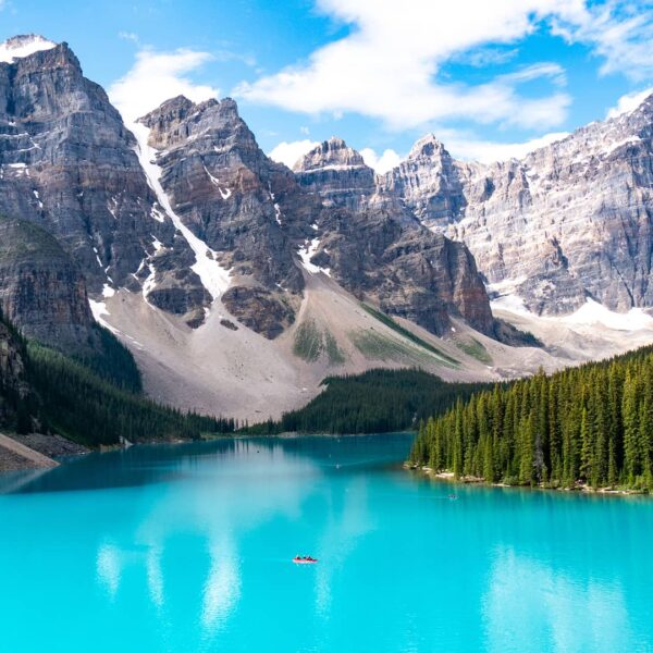 Turquoise waters of Moraine Lake framed by pine forest and dramatic rocky peaks beneath a bright alpine sky.