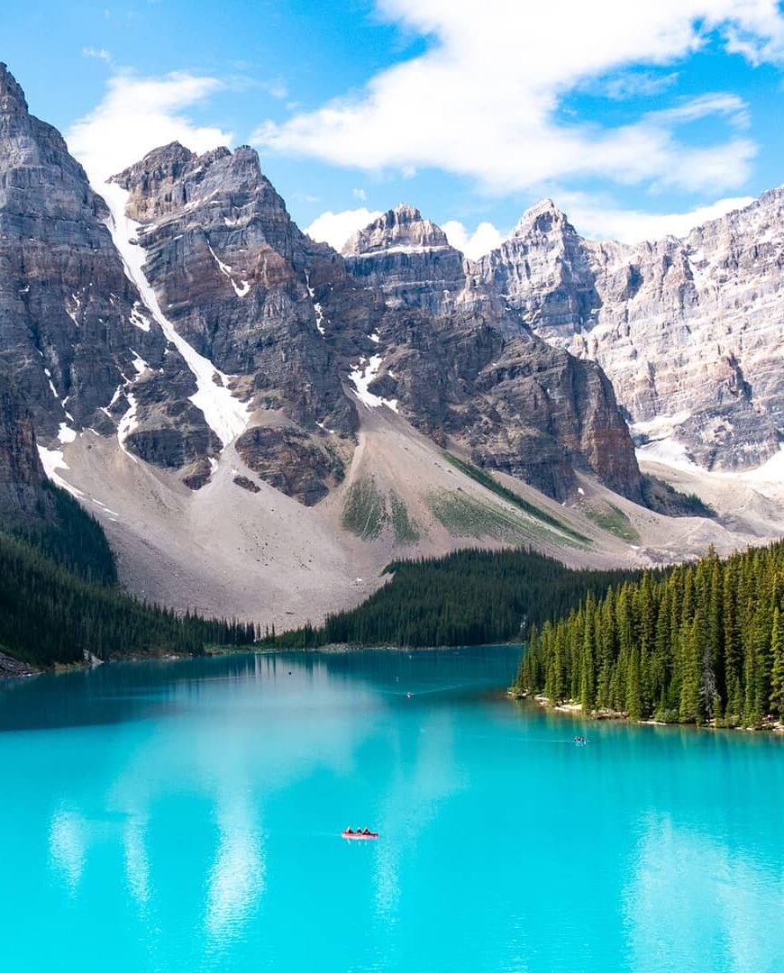 Turquoise waters of Moraine Lake framed by pine forest and dramatic rocky peaks beneath a bright alpine sky.