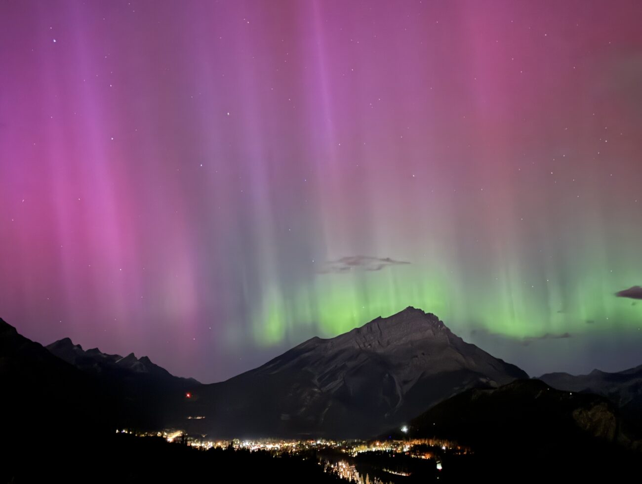 Northern lights glowing above the Bow Valley, viewed from Rimrock Banff, with soft aurora colours illuminating the night sky.
