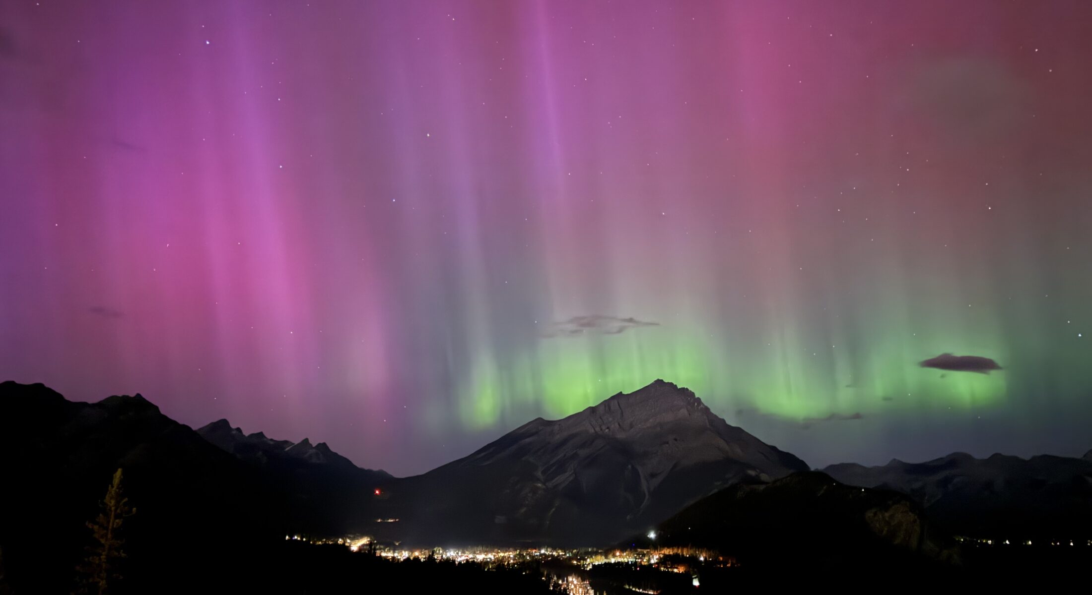 Northern lights glowing above the Bow Valley, viewed from Rimrock Banff, with soft aurora colours illuminating the night sky.