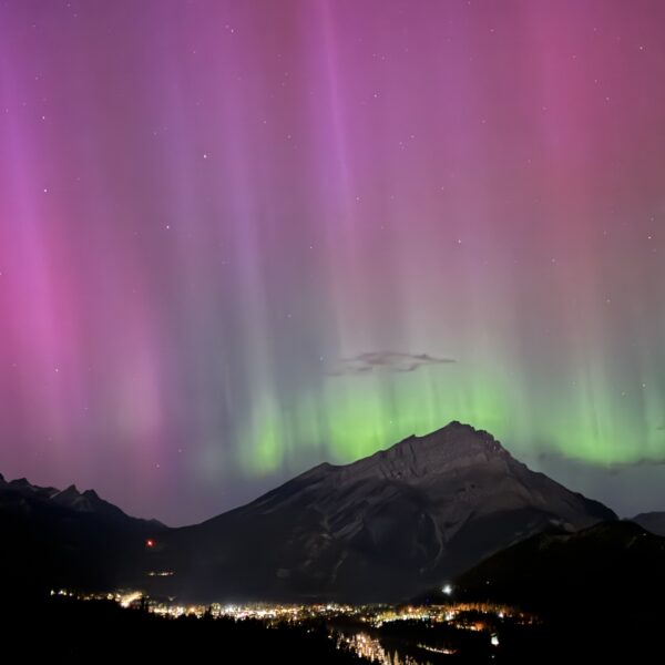 Northern lights glowing above the Bow Valley, viewed from Rimrock Banff, with soft aurora colours illuminating the night sky.