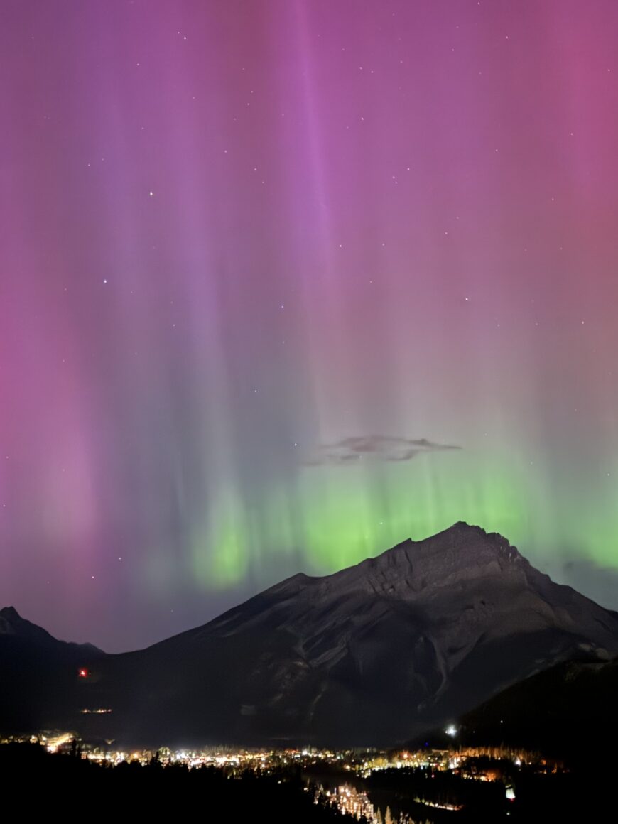 Northern lights glowing above the Bow Valley, viewed from Rimrock Banff, with soft aurora colours illuminating the night sky.