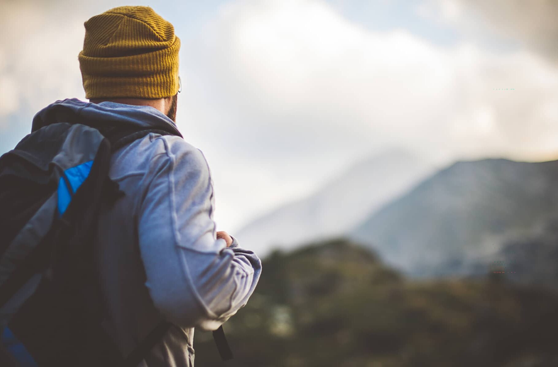 Traveler in Banff National Park with backpack looks on a mountain peak in front of him.