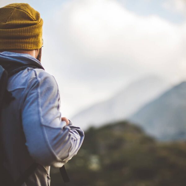 Traveler in Banff National Park with backpack looks on a mountain peak in front of him.