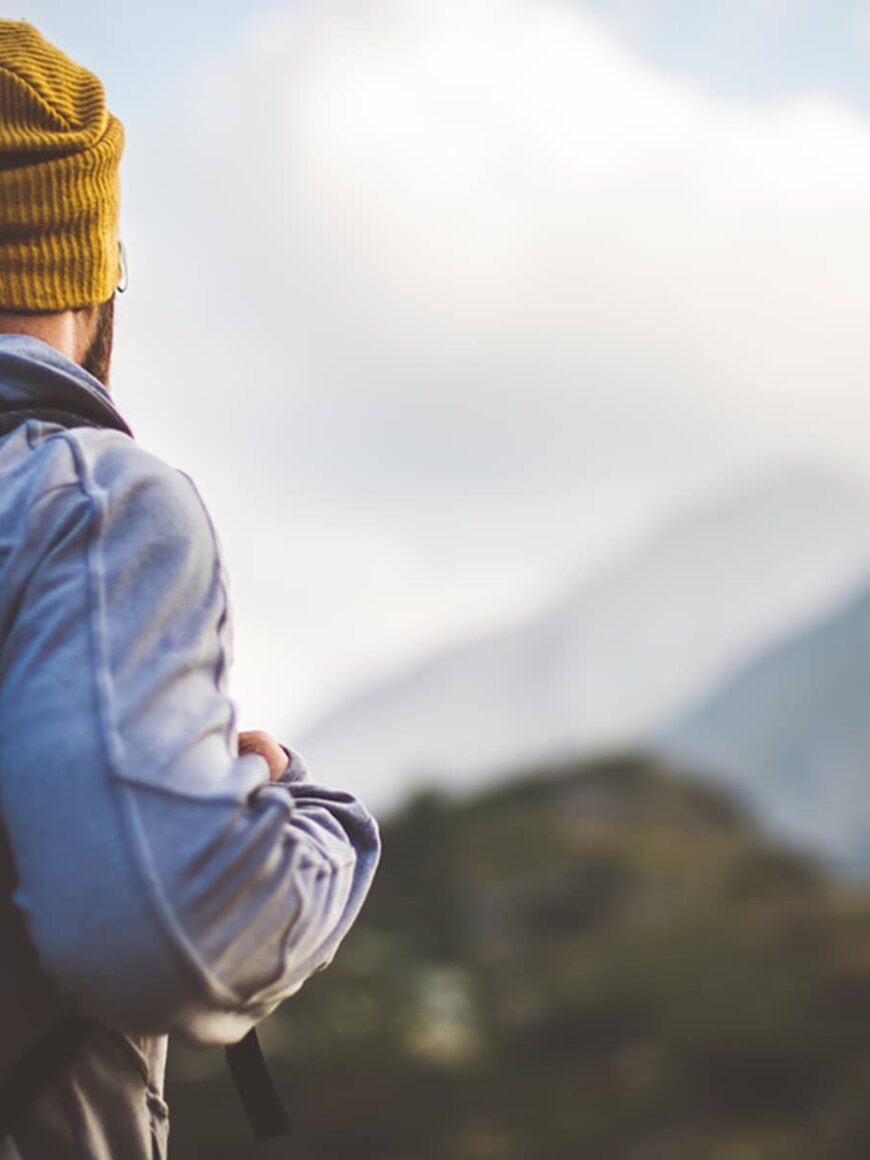 Traveler in Banff National Park with backpack looks on a mountain peak in front of him.