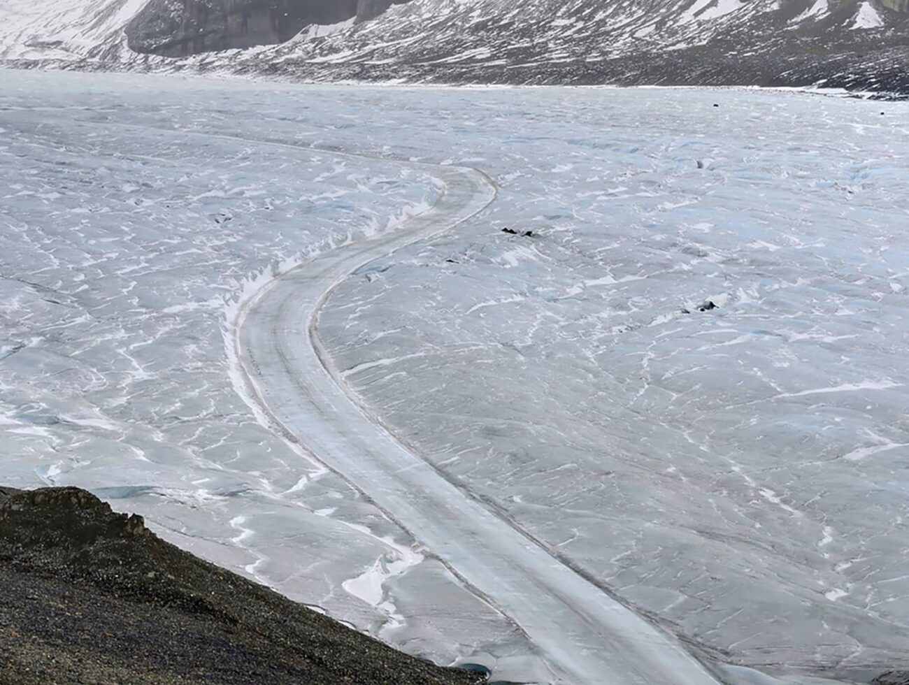 View of the Athabasca Glacier showing a winding track across textured ice, with surrounding rock and alpine slopes.