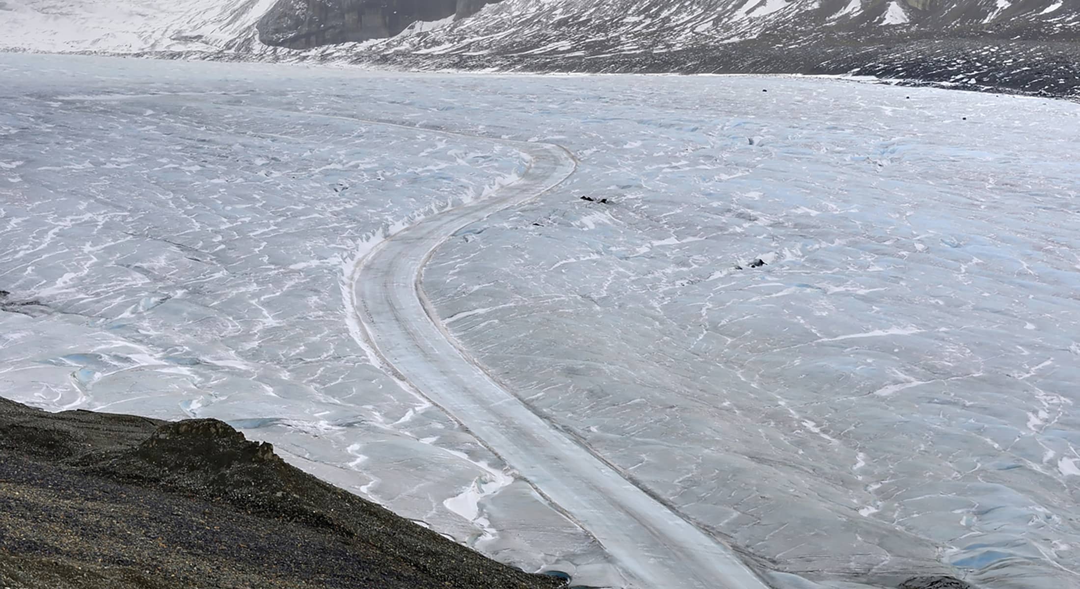 View of the Athabasca Glacier showing a winding track across textured ice, with surrounding rock and alpine slopes.