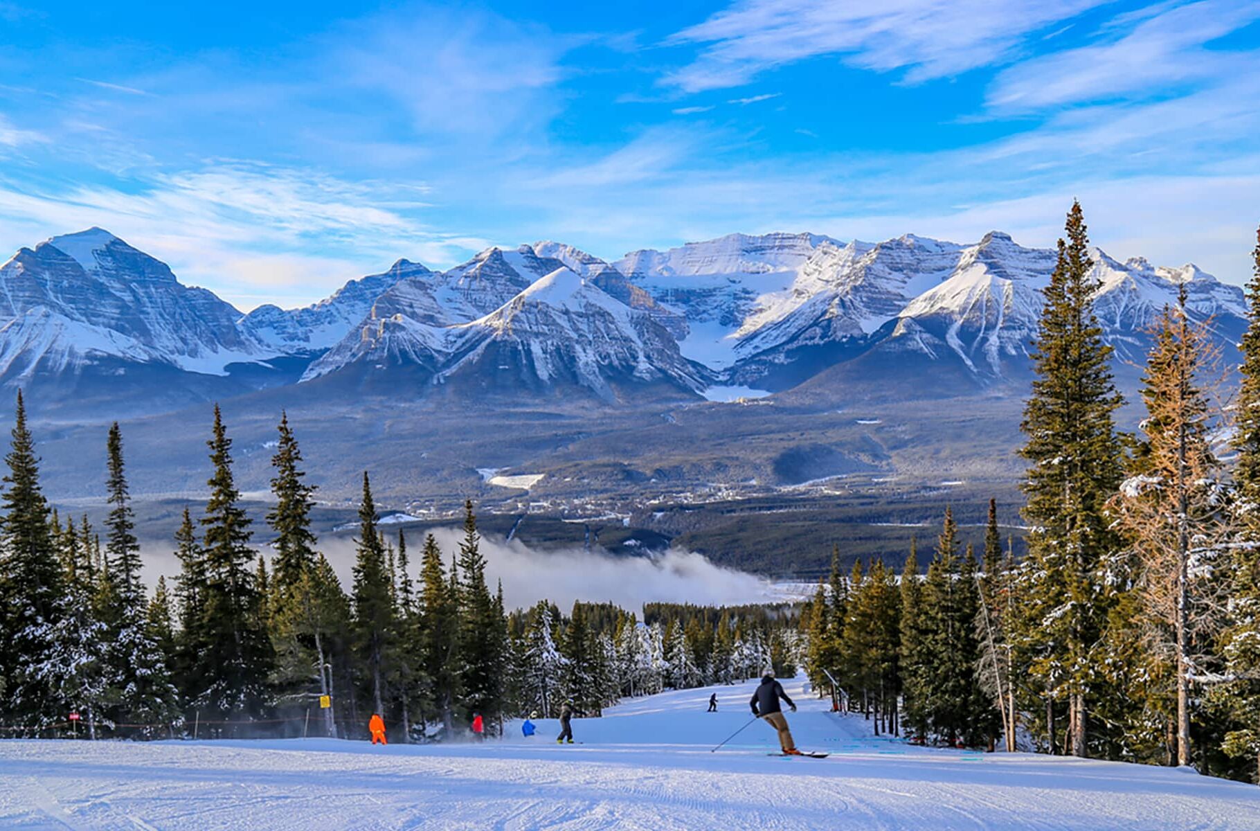 A wide winter view of ski terrain in Banff National Park, with groomed runs, distant peaks, and open alpine landscape.