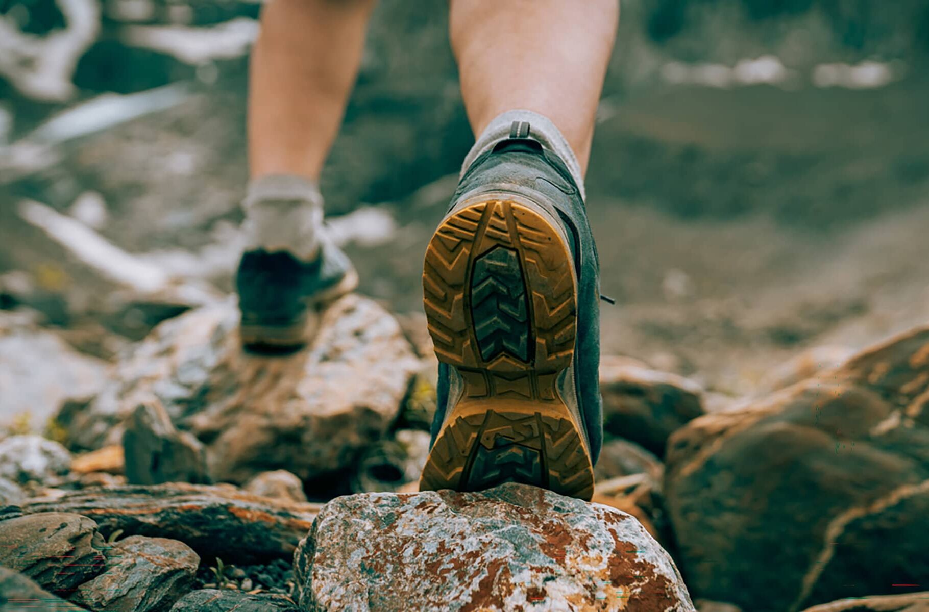 Close-up of hiking boots stepping across uneven rocky terrain on a mountain trail.