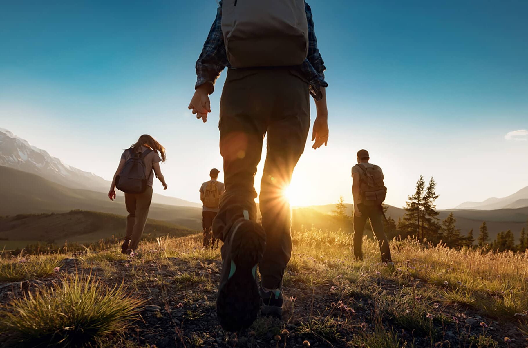 Group of hikers walking across an open ridge at sunset, silhouetted against warm evening light.