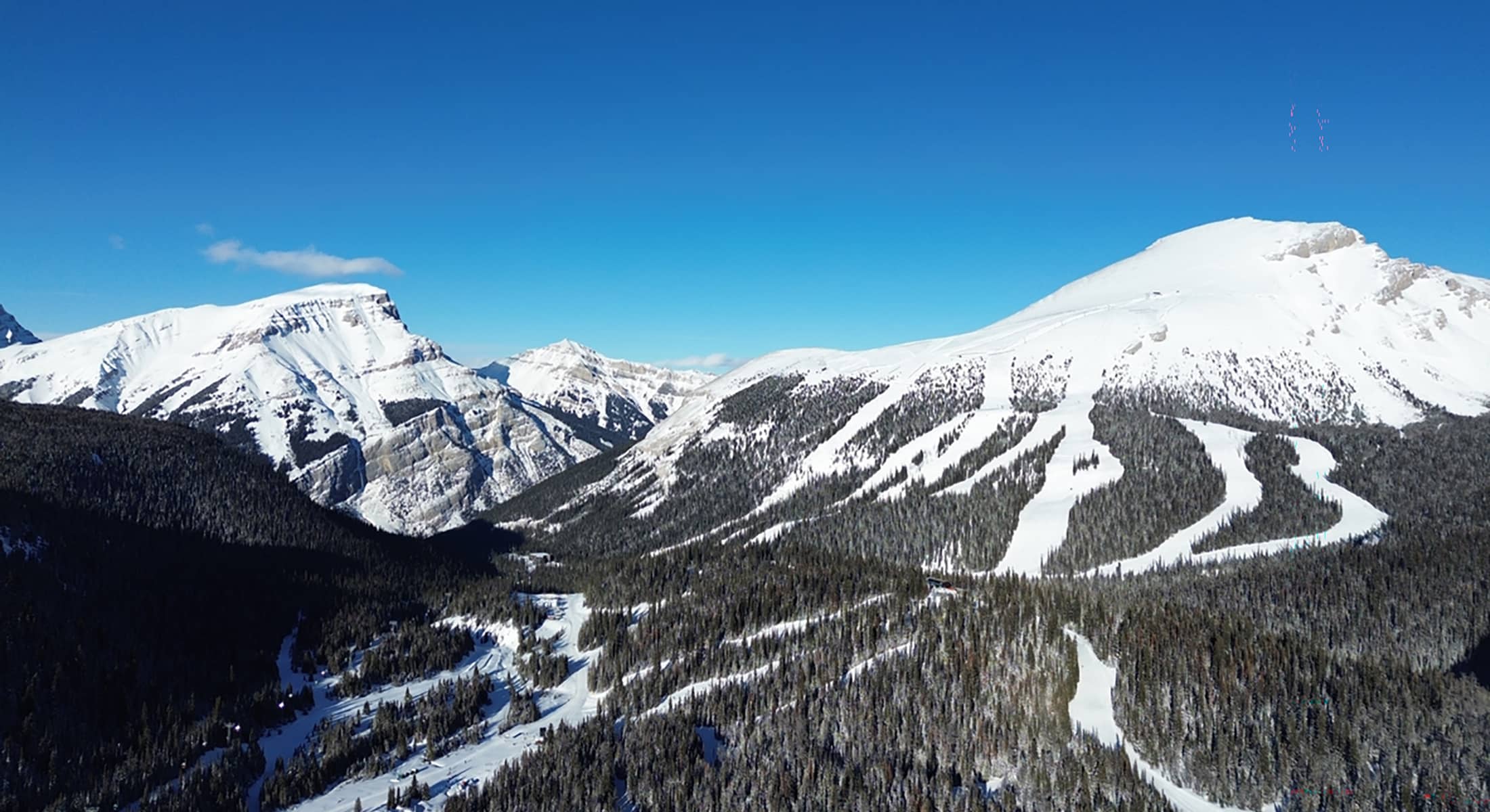 Aerial view of Sunshine Village showing snow-covered alpine ski runs and forested terrain under clear winter skies.