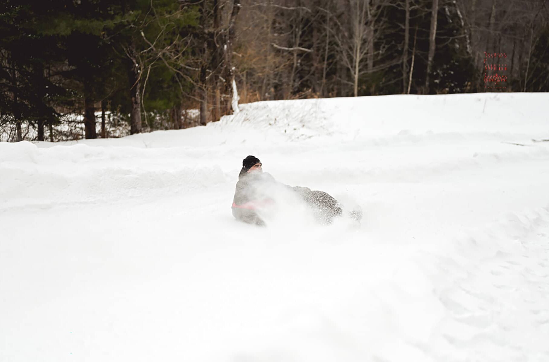 A person snow tubing down a groomed winter lane surrounded by snow-covered trees.