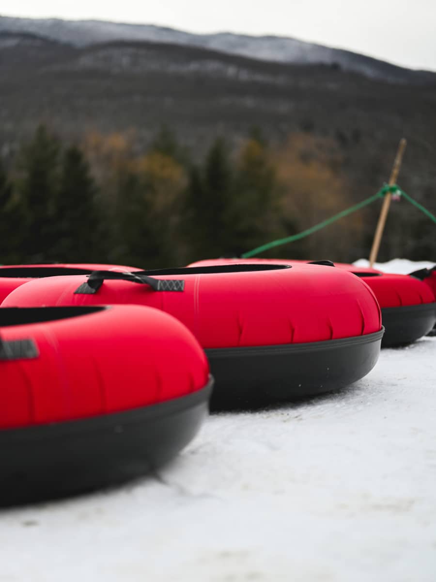 Bright red snow tubes lined up at a tubing area with winter hills in the background.