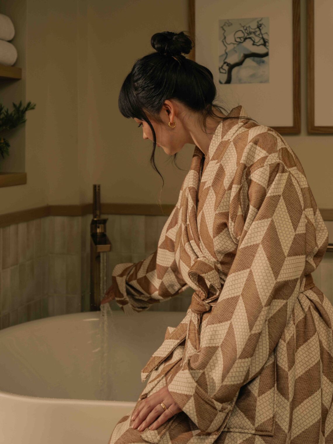 Luxury travel at it's finest with a woman staying at a suite at Rimrock Banff, sitting on the side of her soaker tub in a robe before taking a bath.