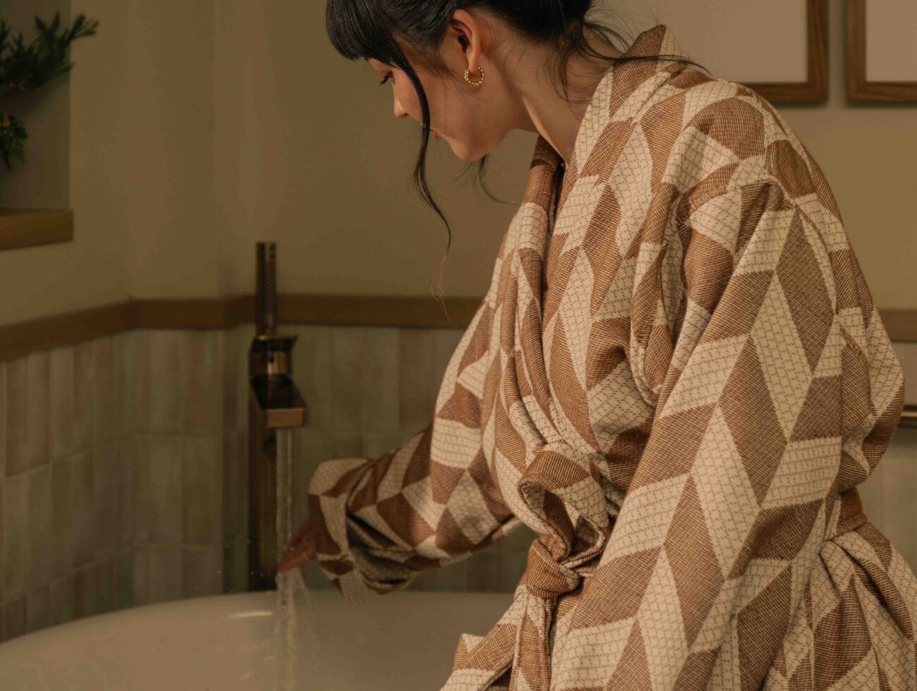 A woman staying at a suite at Rimrock Banff, sitting on the side of her soaker tub in a robe before taking a bath.