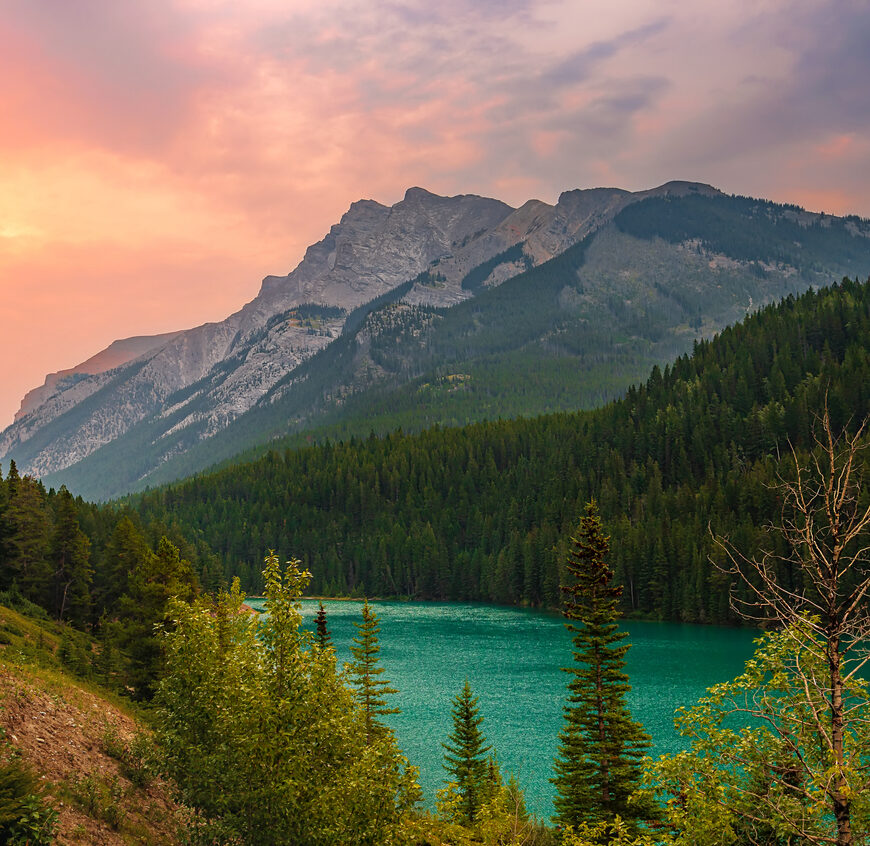 A panoramic sunrise glowing over mountains at Two Jack Lake in the summertime.