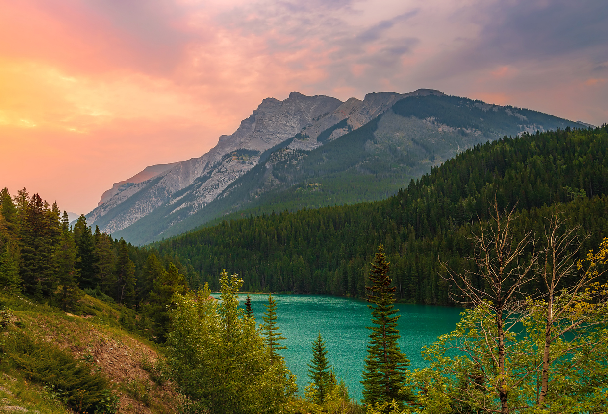 A panoramic sunrise glowing over mountains at Two Jack Lake in the summertime.