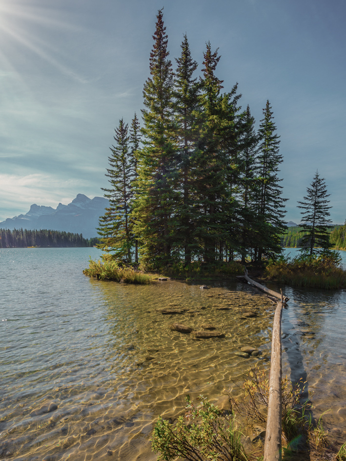 The warm morning sun warms the picturesque lake and a small island. Golden Autumn in Canada. Lake Two Jack in the Rocky Mountains. The concept of ecological and active tourism