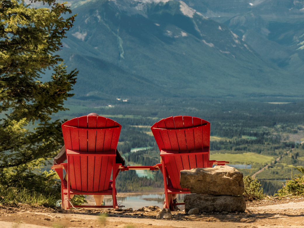 Two people relax in red chairs overlooking Tunnel Mountain in Banff