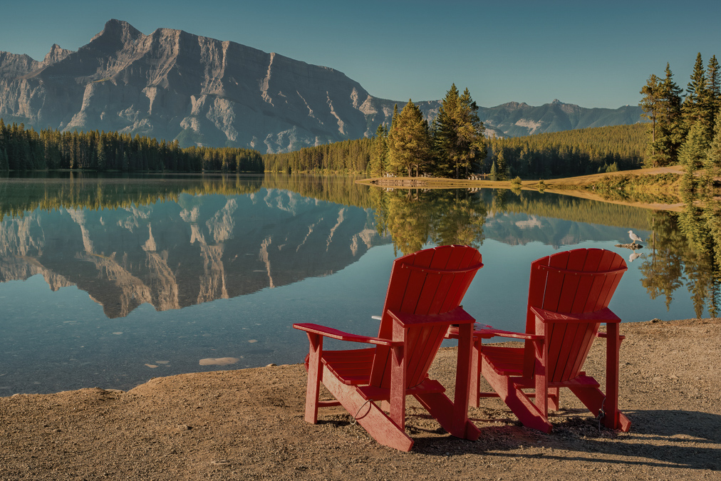 Tranquil landscape with Mt Rundle reflecting in Two Jack Lake, Banff National Park, Alberta Canada on a sunny morning featuring red chairs.