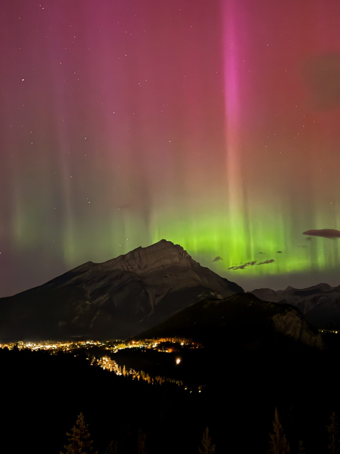 Northern lights glowing above the Bow Valley, viewed from Rimrock Banff, with soft aurora colours illuminating the night sky.