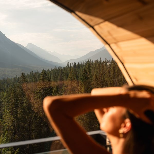 A woman with her fingers in her hair inside of the sauna at Rimrock Banff overlooking Spray Valley.